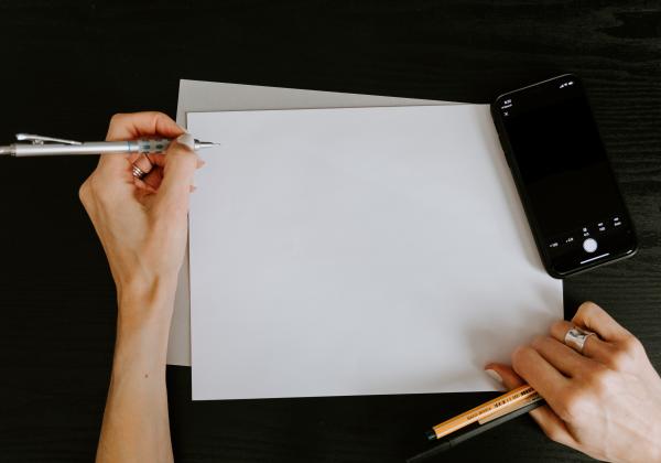 A hand with a pen over a blank piece of paper