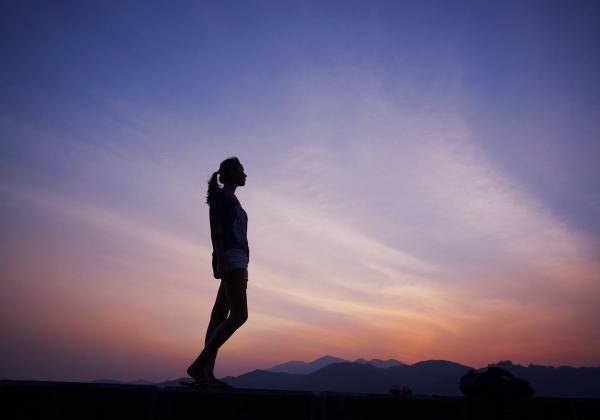 A woman's silhouette in front of a pale sunset